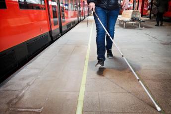 Henkilö kävelee valkoisen kepin kanssa metroasemalla